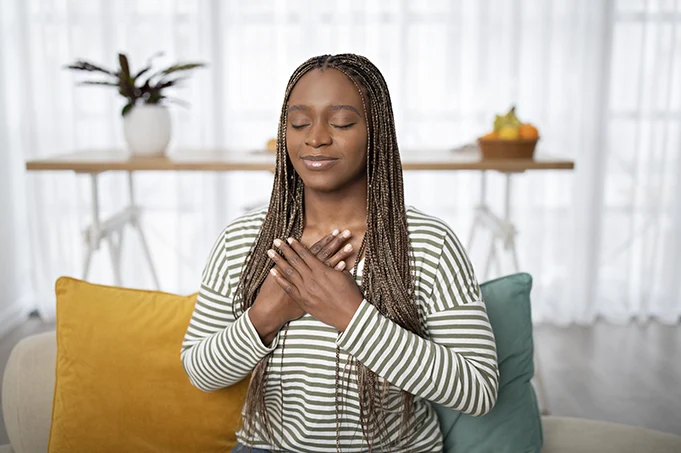 Woman seated indoors with hands on her heart, representing online embodied transformation and somatic integration.