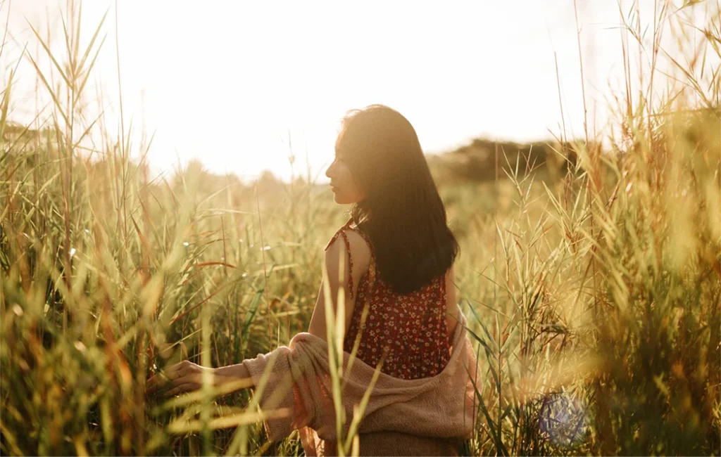Woman sitting quietly in a sunlit field, representing embodied healing and nervous system regulation.