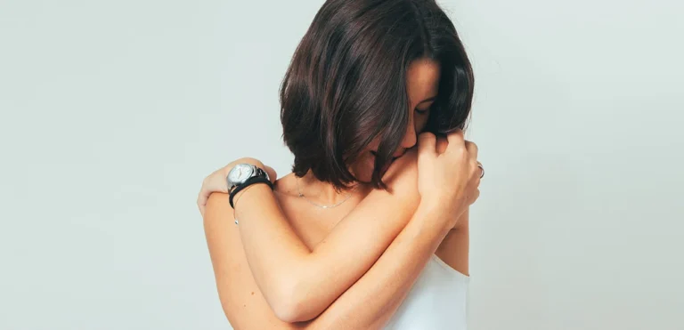 Woman holding herself in a quiet moment of reflection, representing somatic healing and emotional patterns.